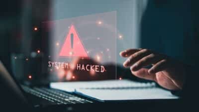 Cyber security warning displayed on a laptop screen with a red alert icon and the message 'System Hacked', highlighting the cost of a cyber attack or security breach. Cyber security warning displayed on a laptop screen with a red alert icon and the message 'System Hacked', highlighting the cost of a cyber attack or security breach.